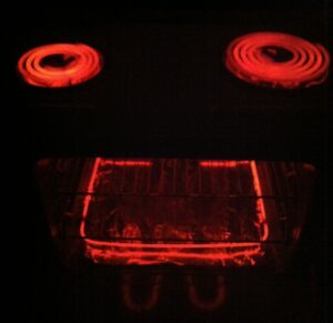 A red screaming face against a black background, consisting of two round stove elements as eyes and a rectangular oven element as a mouth