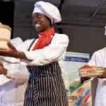 A Black woman and man wearing chefs' uniforms stand holding out baskets of healthy food.