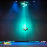 A photo of a projection on the theatre curtain, depicting a human figure falling underwater