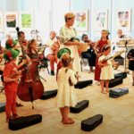 The conductor, the singer (Musica), the two choirs of children playing violin, the string orchestra