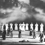 A black and white photo of several actors in robes gathered on a large stage
